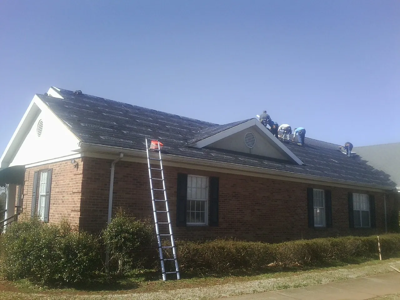 Crew tearing shingles off a brick ranch roof with a ladder set — Metal Roof Repair work by our crew in Bryant